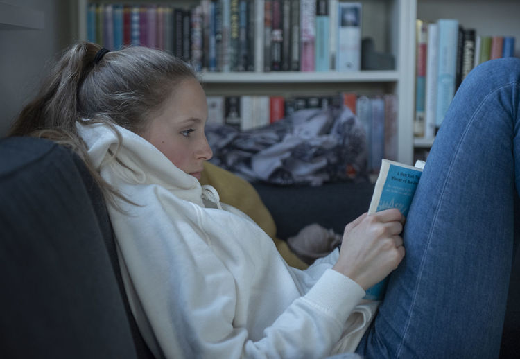 Teenager girl reading book while sitting at home
