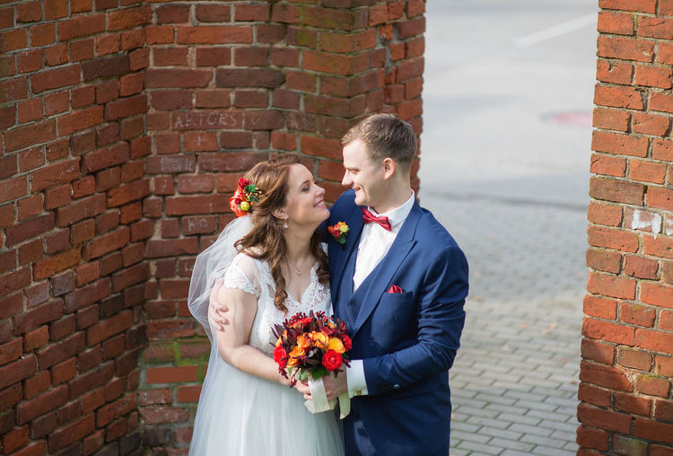 Bride and groom standing by brick wall