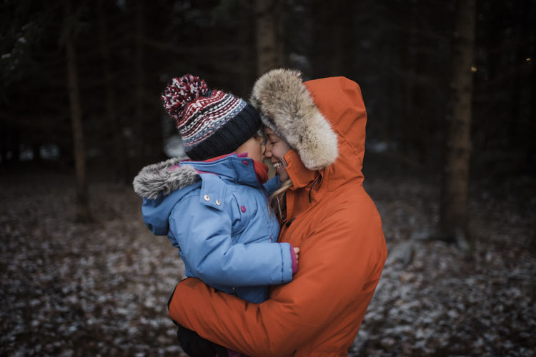 Happy mother carrying daughter while standing in forest during winter