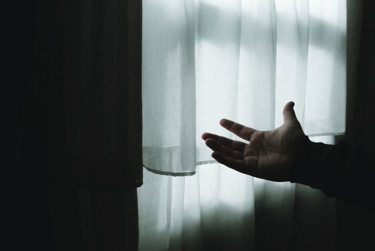 Cropped hand of man reaching for window curtain in darkroom