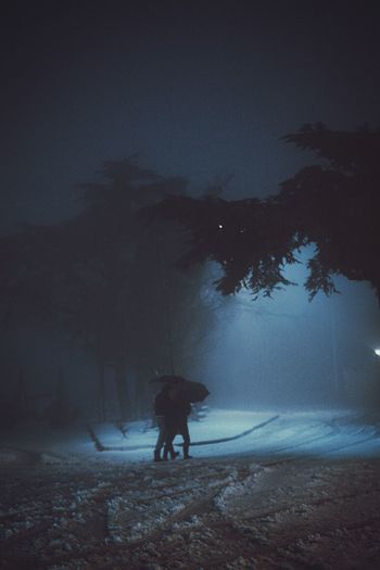 Two persons walking on snow covered land against sky at night