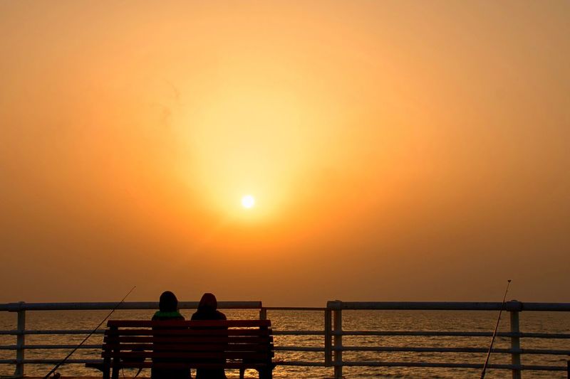 Silhouette people standing on beach against orange sky