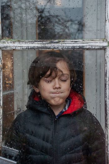 Portrait of boy in wet glass window