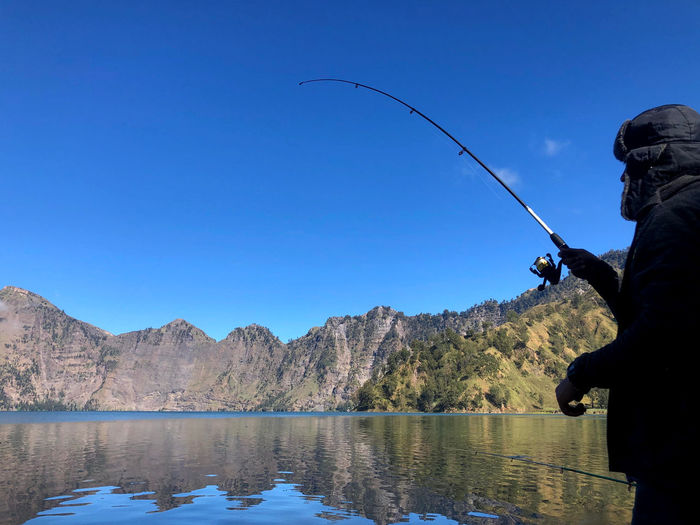 Man fishing in lake against blue sky