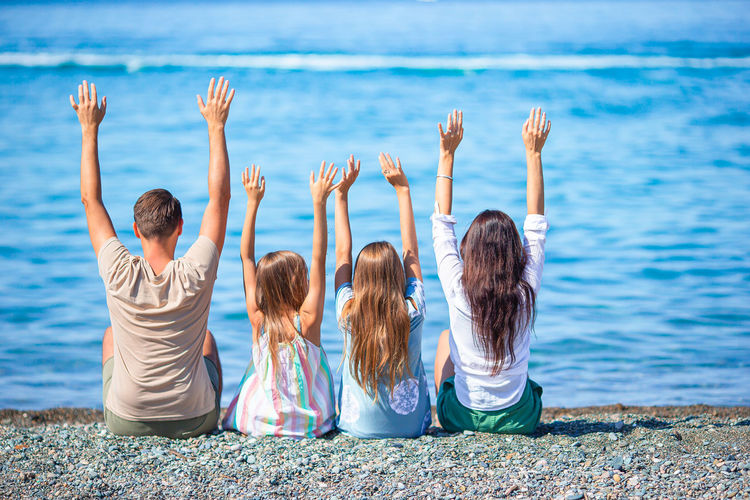Rear view of family with arms raised on beach