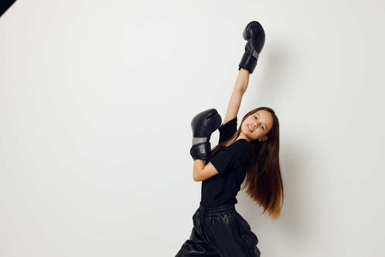 Portrait of girl wearing boxing gloves standing against white background