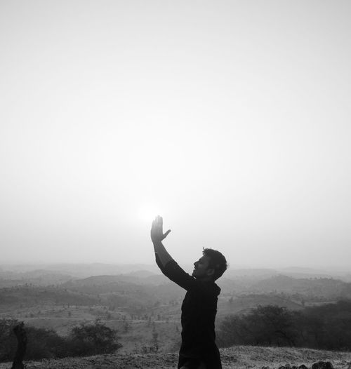Man standing with arms raised against sky