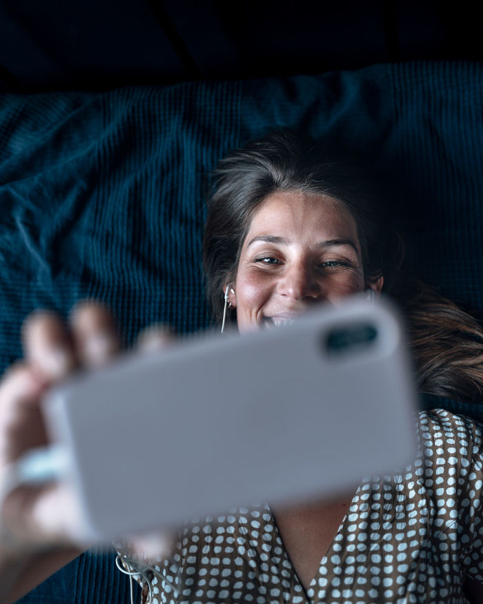 Directly above shot of woman on video call while lying in bed