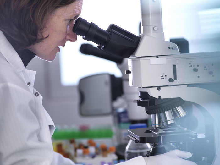 Side view of female scientist analyzing blood samples through microscope in laboratory