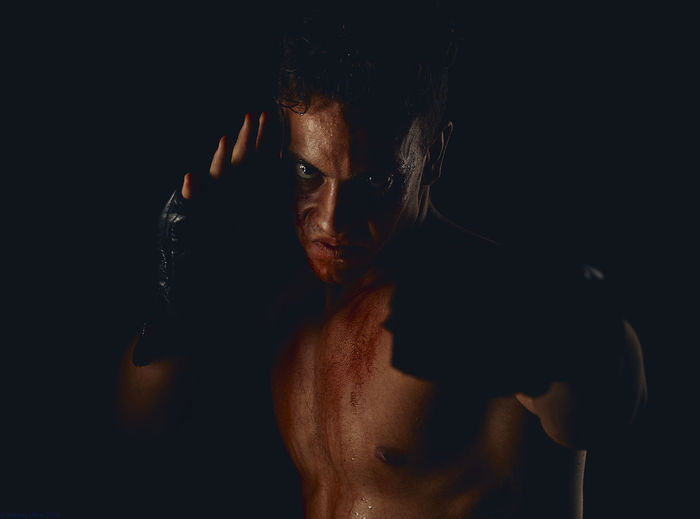 Close-up portrait of shirtless man wearing boxing glove in darkroom