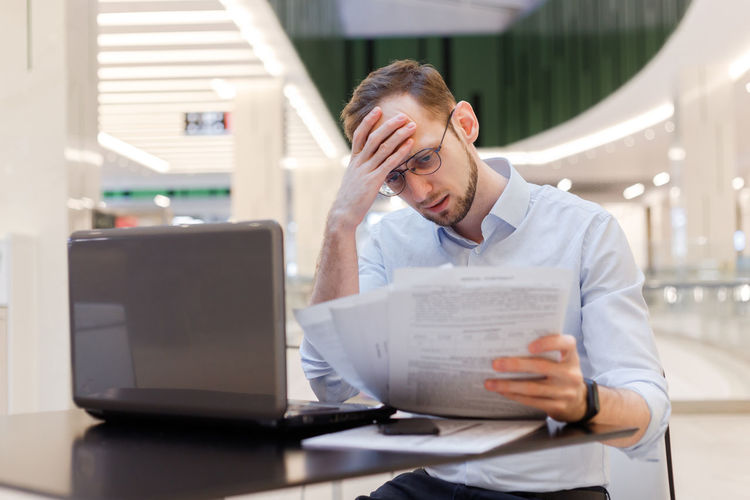 Depressed businessman reading document while sitting at mall