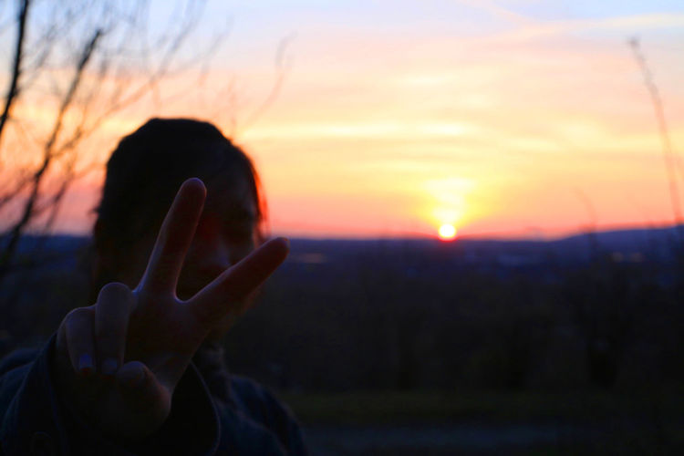 Close-up of human hand against sunset sky