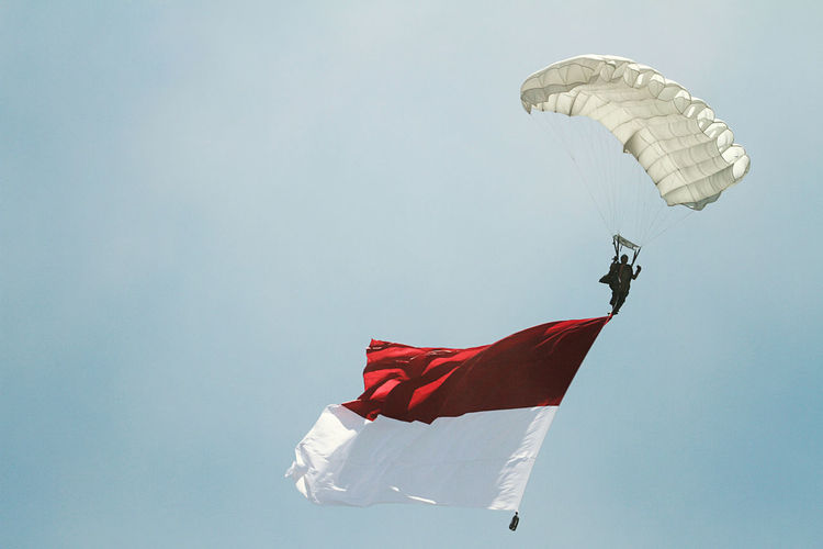 Low angle view of man with flag paragliding against clear sky