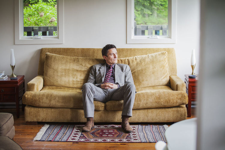 Thoughtful man looking away while sitting on sofa at home