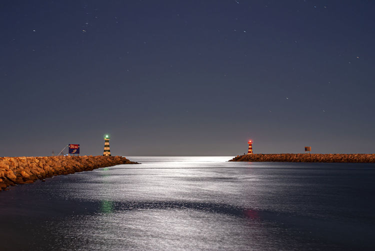 Lighthouse by sea against clear sky at night