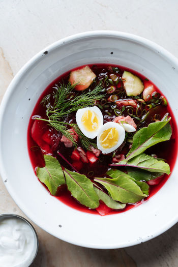 From above palatable red beetroot soup with boiled eggs and herbs in white plate on table