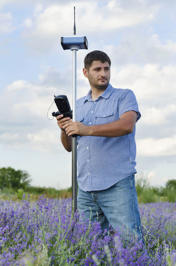 Surveyor using equipment on lavender field against cloudy sky