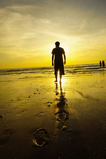 Rear view of silhouette man on beach against sky during sunset