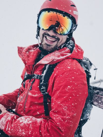 Portrait of smiling man in red jacket standing in snow