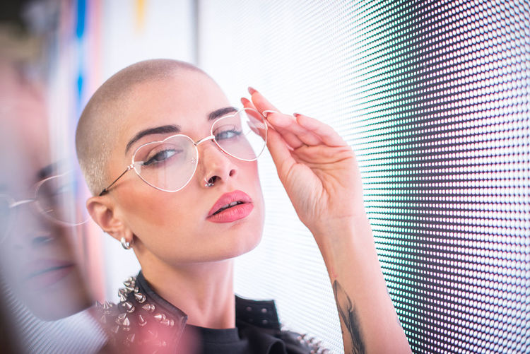 Portrait of young woman with shaved head standing against abstract backgrounds