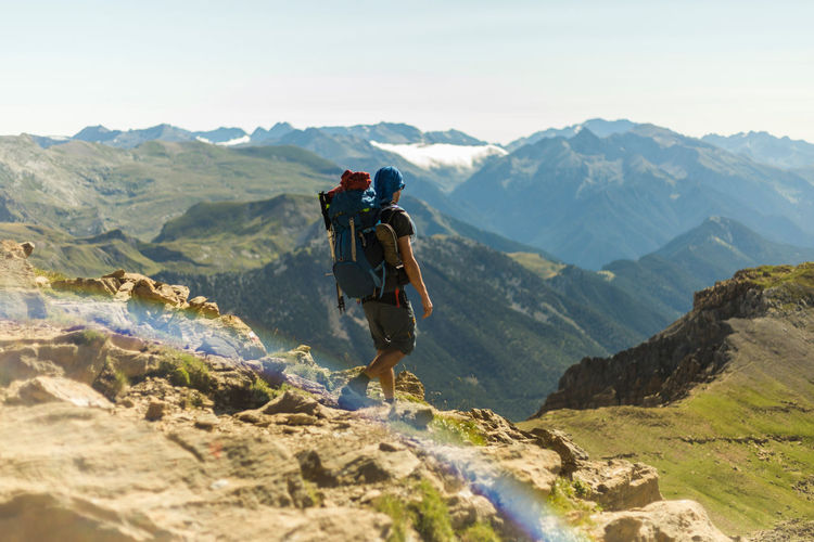 Unrecognizable man with backpack walking and admiring mountain range on sunny day in pyrenees