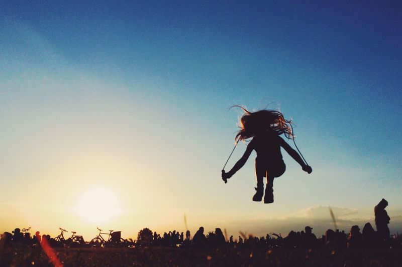 Silhouette girl jumping in park against clear sky at sunset