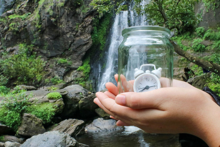 Cropped image of hand holding rock in waterfall