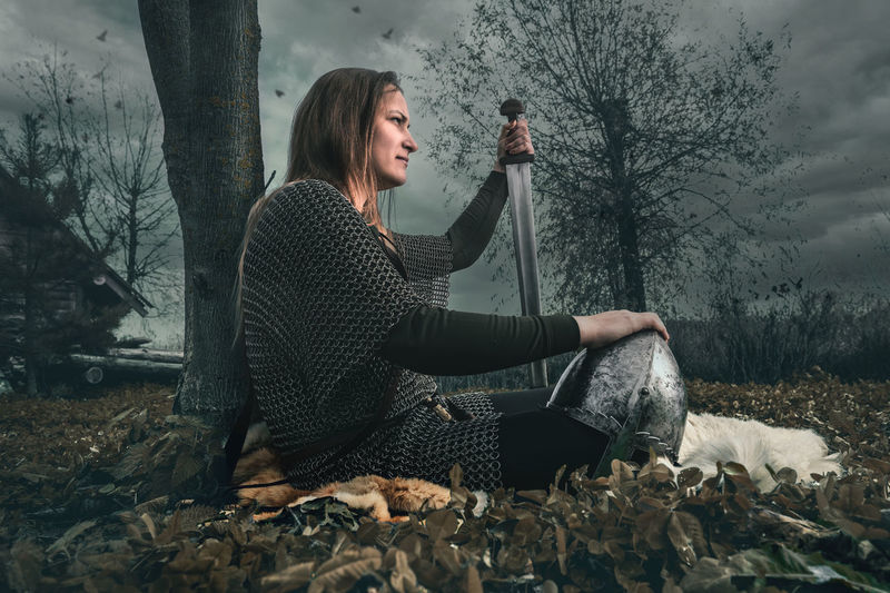 Woman warrior in chain mail.  a woman warrior in chain mail sits near a tree after a battle.