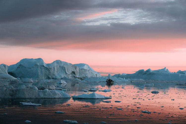 Boat moored amidst icebergs on sea against sky during sunset