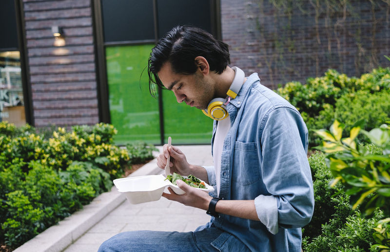 Man eating salad sitting by plants