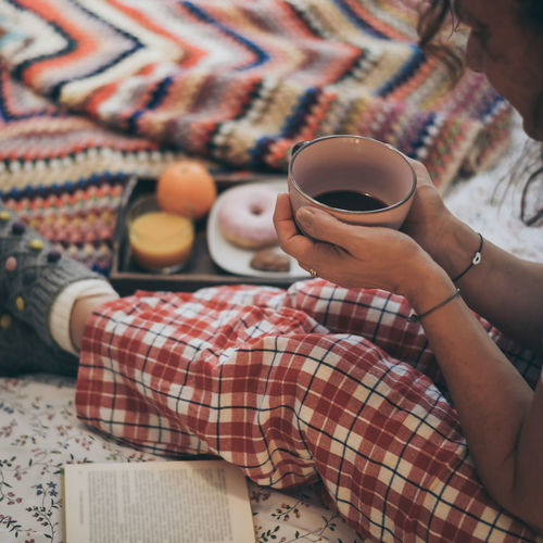 Midsection of woman holding coffee cup on bed
