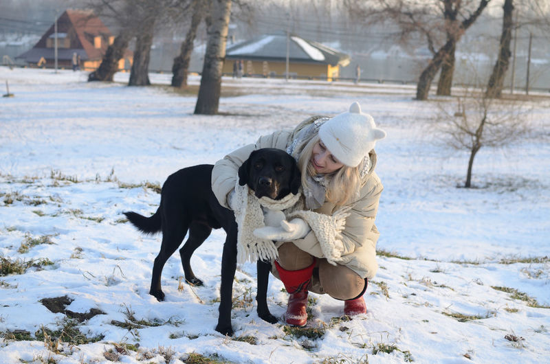 Woman in winter clothes hugging beautiful black dog on winter day