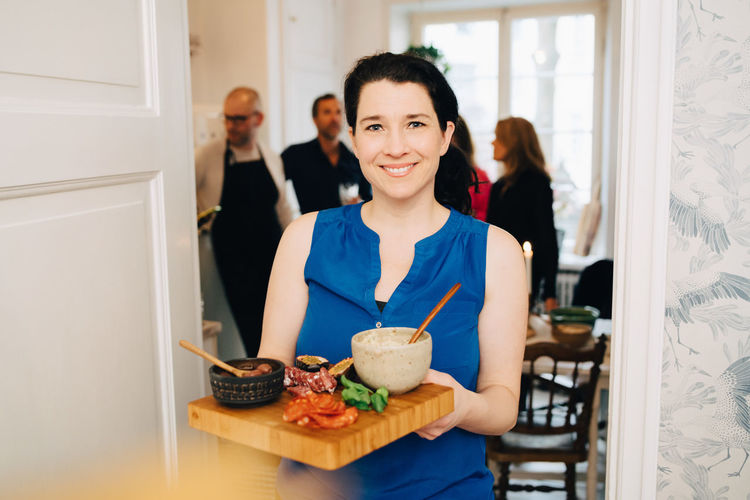 Portrait of smiling woman holding serving tray while standing at doorway in party