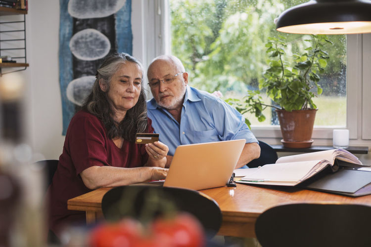 Senior couple using credit card for online payment on laptop at home
