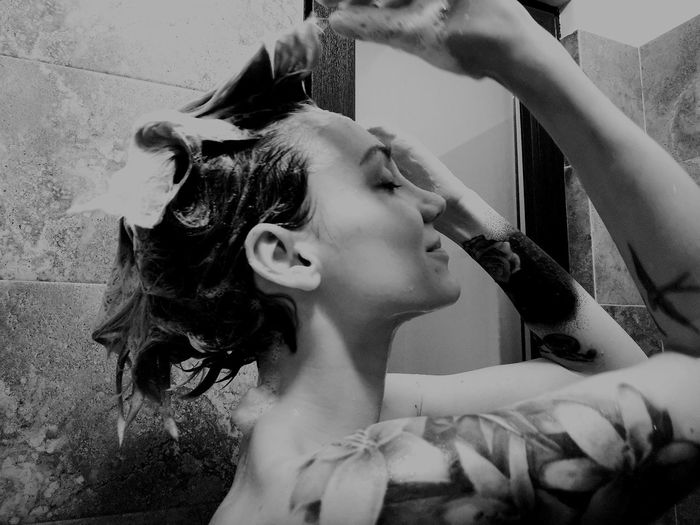 Side view of smiling young woman applying shampoo in hair at bathroom