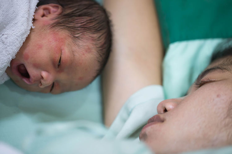 Close-up of baby boy sleeping by mother on bed in hospital