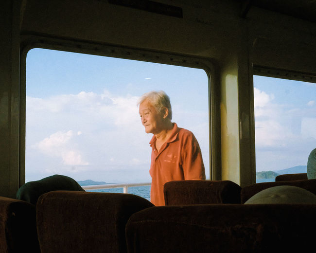 Mature man against cloudy sky seen through ferry window