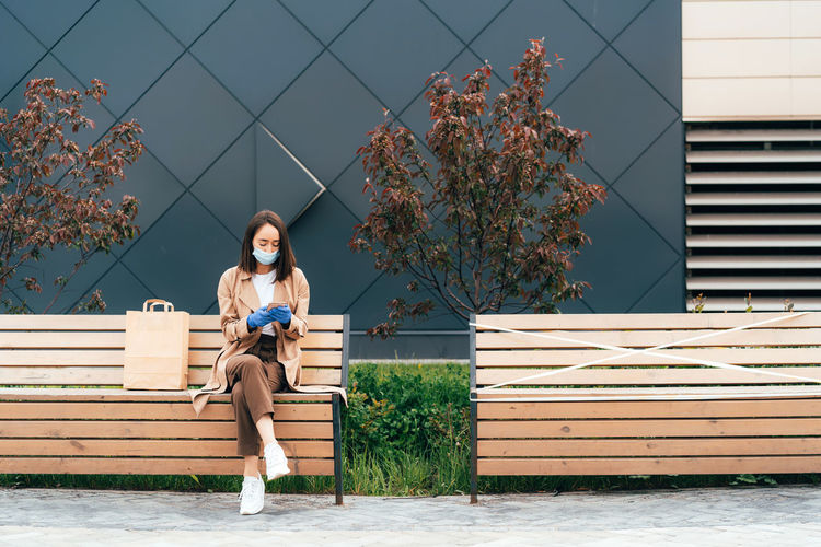 Woman in protective  mask and gloves using smartphone. physical social distancing.