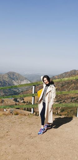 Full length portrait of young woman sitting on mountain against sky