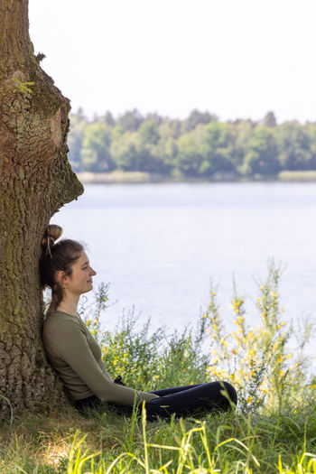 Side view of woman sitting on rock by lake