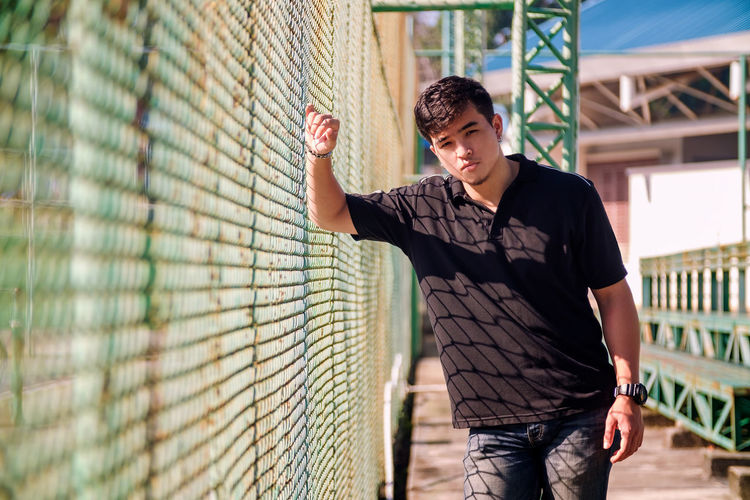 Portrait of young man standing against chainlink fence