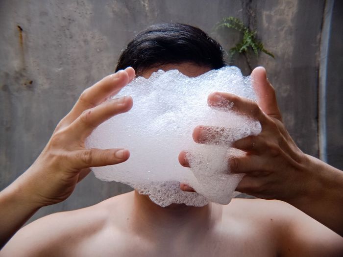Close-up of shirtless man holding soap sud