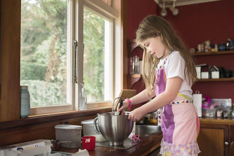 Young girl wearing an apron and baking in a messy kitchen