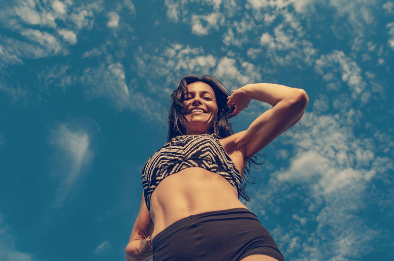 Woman athletic physique, sports shorts, top. bottom view on blue sky background.