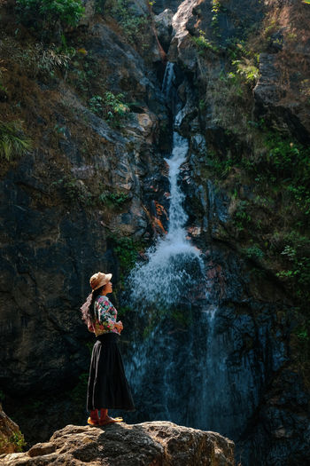 Woman standing on rock against waterfall in forest