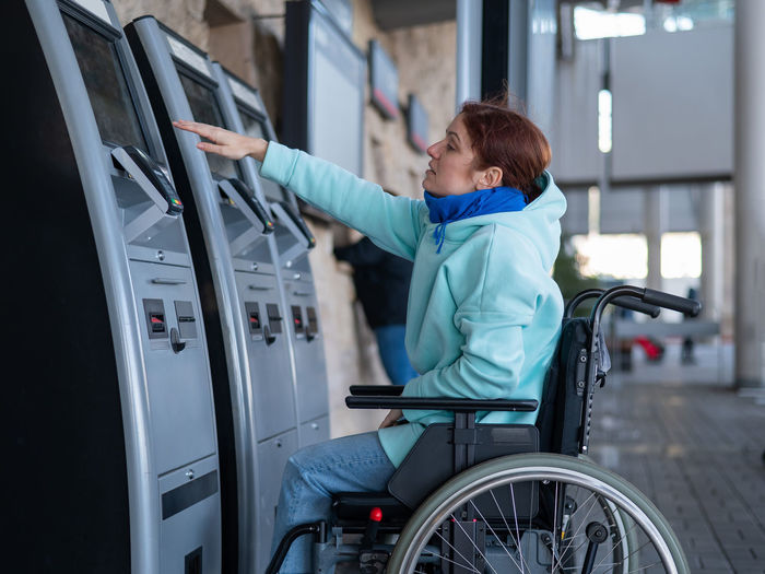 Disabled woman on wheelchair at ticket vending machine
