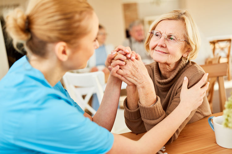 Female caregiver consoling senior woman in nursing home