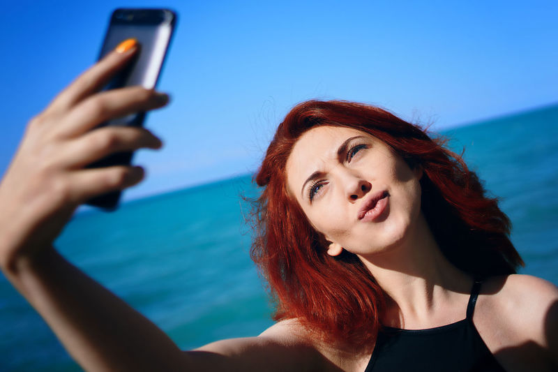 Portrait of young woman using mobile phone against sky