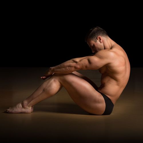 Side view of muscular athlete exercising on hardwood floor