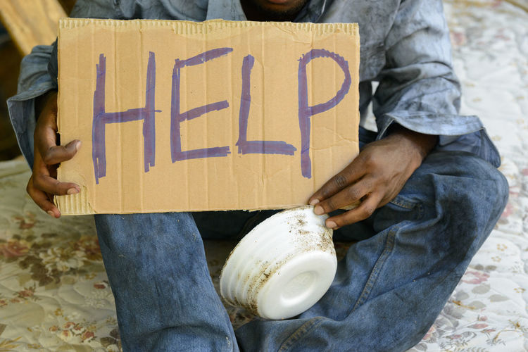 Midsection of beggar holding cardboard with text